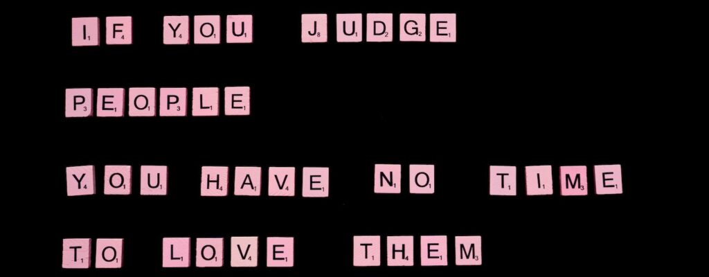 If You Judge People You Have No Time To Love Them text spelled out with pink letter tiles of famous word game against black background