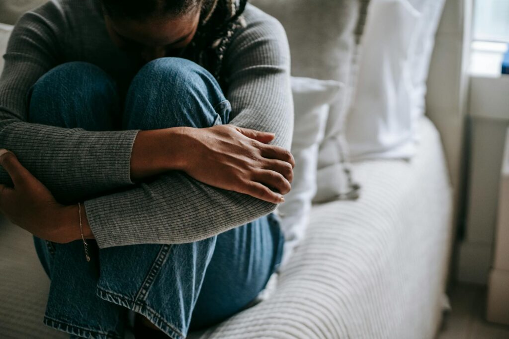 Crop pitiful black woman embracing knees on bed